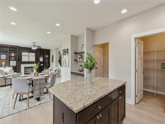 kitchen featuring ceiling fan, a center island, light stone countertops, dark brown cabinets, and light wood-type flooring