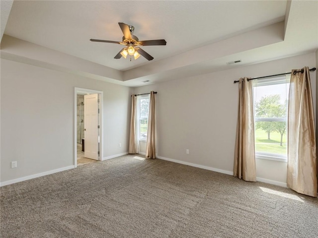 carpeted spare room with a raised ceiling and ceiling fan