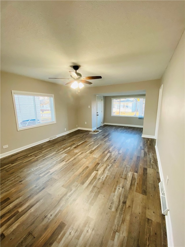 unfurnished living room with a textured ceiling, dark wood-type flooring, and ceiling fan