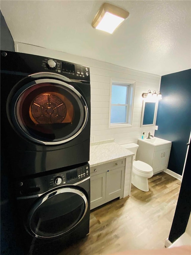 laundry room with sink, wood-type flooring, and stacked washer / drying machine