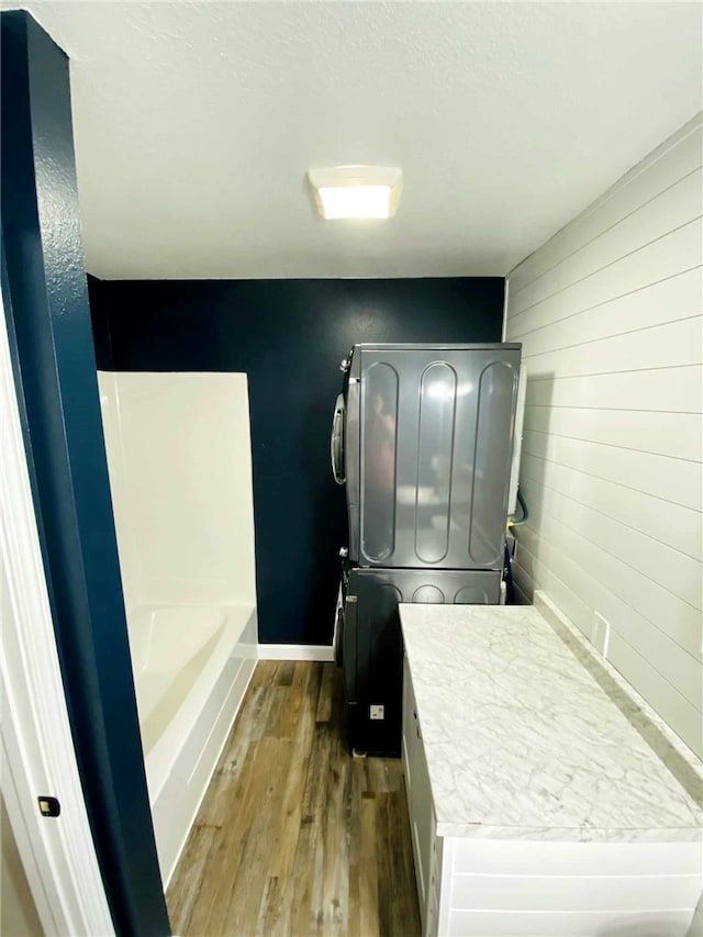 bathroom featuring a tub, stacked washing maching and dryer, and wood-type flooring