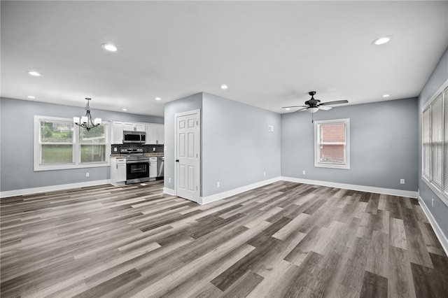 unfurnished living room featuring ceiling fan with notable chandelier and light hardwood / wood-style floors