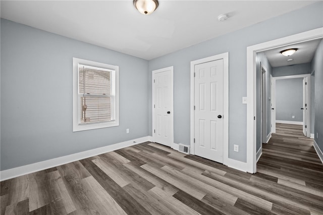 unfurnished bedroom with two closets and dark hardwood / wood-style floors