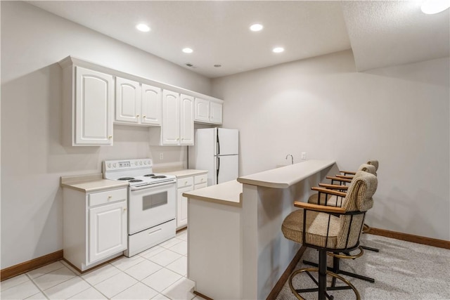 kitchen featuring a kitchen breakfast bar, light tile patterned flooring, kitchen peninsula, white appliances, and white cabinets