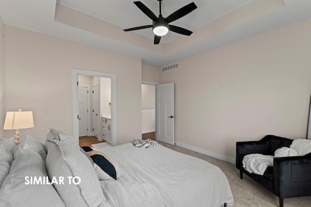 bedroom with ceiling fan, ensuite bath, and a tray ceiling