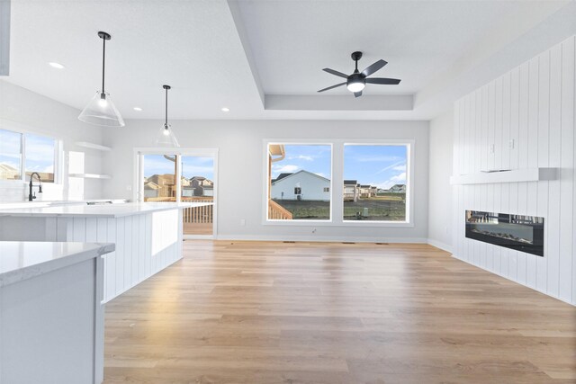 unfurnished living room featuring ceiling fan, sink, a raised ceiling, and light hardwood / wood-style floors