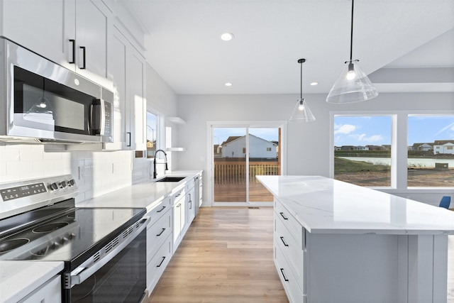 kitchen featuring backsplash, stainless steel appliances, white cabinets, a kitchen island, and decorative light fixtures