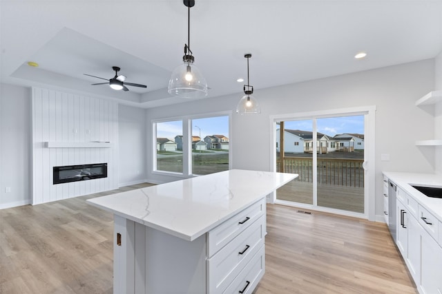 kitchen featuring a center island, a tray ceiling, a large fireplace, white cabinets, and decorative light fixtures