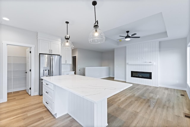 kitchen featuring stainless steel fridge, white cabinetry, a large fireplace, a kitchen island, and a raised ceiling