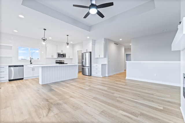 kitchen featuring a kitchen island, appliances with stainless steel finishes, white cabinetry, hanging light fixtures, and light wood-type flooring