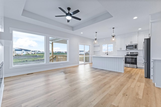 kitchen featuring a center island, hanging light fixtures, a tray ceiling, stainless steel appliances, and white cabinets