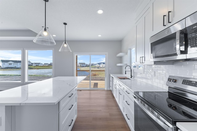 kitchen featuring white cabinetry, hanging light fixtures, stainless steel appliances, a water view, and a kitchen island