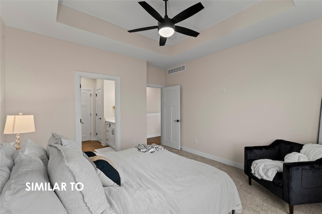 bedroom with ceiling fan, connected bathroom, a raised ceiling, and light carpet