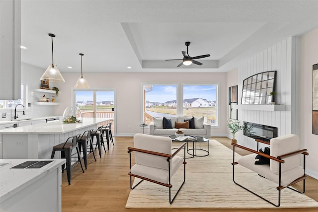 living room featuring ceiling fan, sink, light wood-type flooring, and a tray ceiling