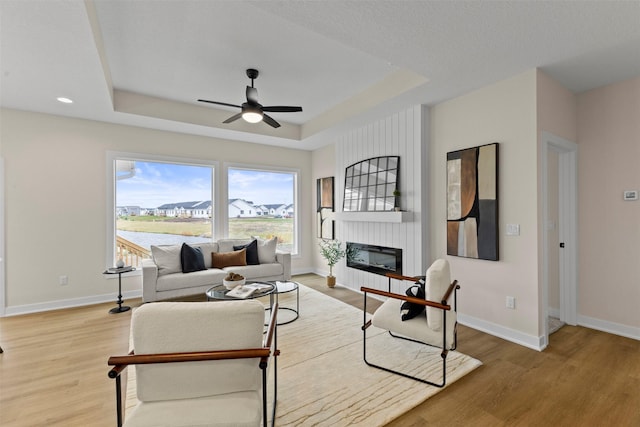 living room with a raised ceiling, ceiling fan, hardwood / wood-style floors, and a fireplace