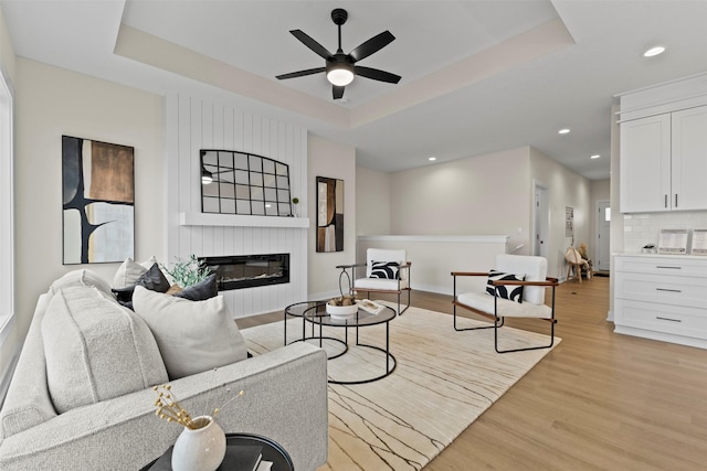 living room featuring a tray ceiling, ceiling fan, and light wood-type flooring