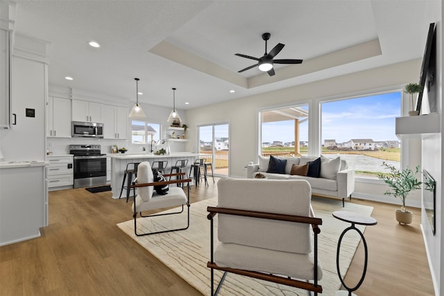 living room with ceiling fan, a tray ceiling, and light hardwood / wood-style floors