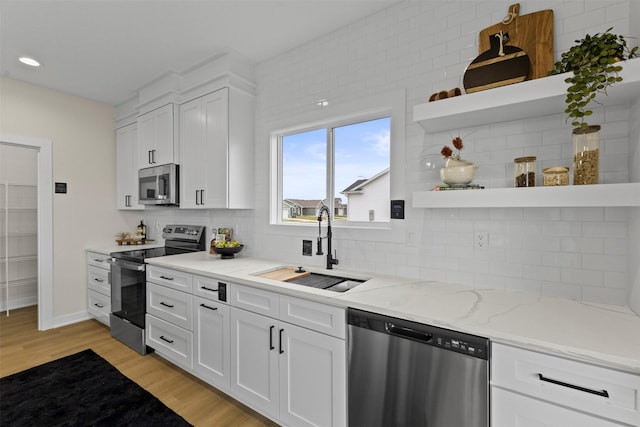 kitchen featuring sink, white cabinets, light stone counters, stainless steel appliances, and light hardwood / wood-style flooring