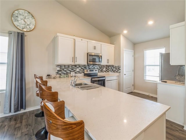 kitchen with decorative backsplash, vaulted ceiling, dark wood-type flooring, appliances with stainless steel finishes, and white cabinetry