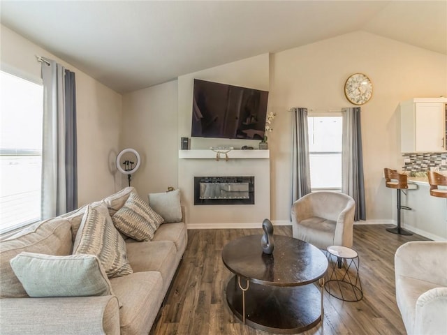 living area featuring wood finished floors, a healthy amount of sunlight, a glass covered fireplace, and vaulted ceiling