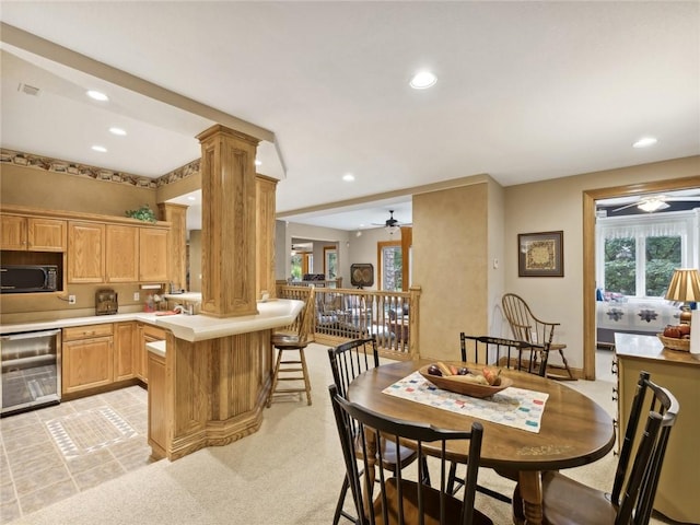 kitchen with a kitchen bar, ceiling fan, ornate columns, light colored carpet, and beverage cooler