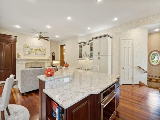 kitchen with light stone countertops, a kitchen breakfast bar, dark hardwood / wood-style flooring, ceiling fan, and a large island