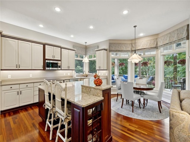 kitchen featuring a kitchen island, dark hardwood / wood-style floors, decorative light fixtures, a breakfast bar area, and white cabinets