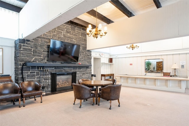 carpeted dining room with a healthy amount of sunlight, beamed ceiling, a high ceiling, a chandelier, and a stone fireplace