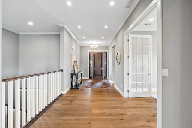 foyer entrance with light wood-type flooring, crown molding, and a chandelier