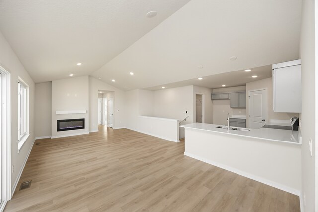 unfurnished living room featuring lofted ceiling, sink, and light hardwood / wood-style flooring