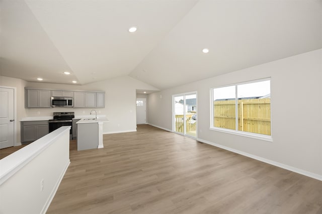 kitchen featuring stainless steel appliances, vaulted ceiling, a center island with sink, light hardwood / wood-style flooring, and gray cabinets