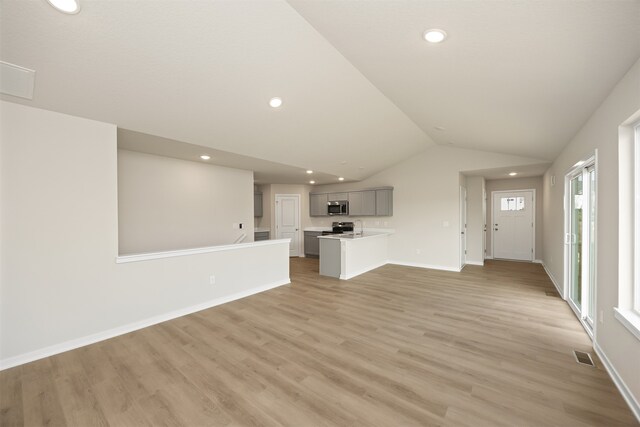 unfurnished living room featuring plenty of natural light, light hardwood / wood-style floors, and vaulted ceiling