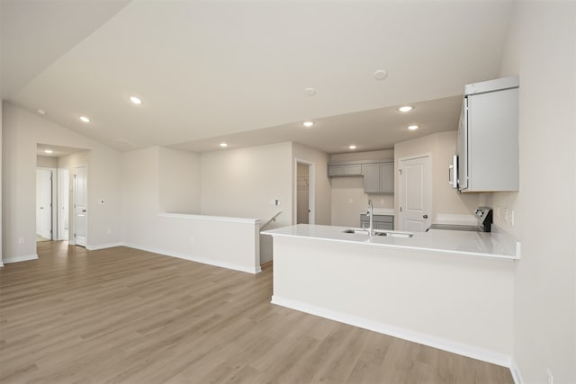 kitchen featuring lofted ceiling, sink, stainless steel stove, light wood-type flooring, and kitchen peninsula