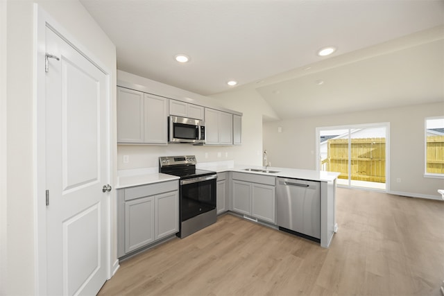 kitchen featuring sink, stainless steel appliances, kitchen peninsula, vaulted ceiling, and light wood-type flooring