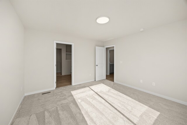 unfurnished bedroom with light colored carpet, a walk in closet, and a closet