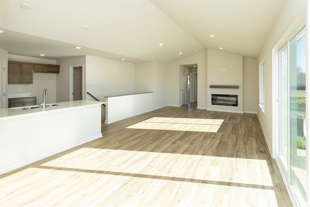 unfurnished living room featuring light wood-type flooring, lofted ceiling, and sink