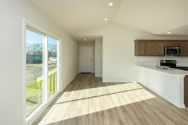kitchen featuring kitchen peninsula, appliances with stainless steel finishes, vaulted ceiling, and light hardwood / wood-style flooring