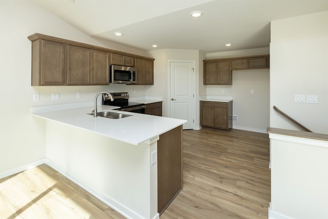 kitchen featuring light wood-type flooring, appliances with stainless steel finishes, kitchen peninsula, sink, and lofted ceiling