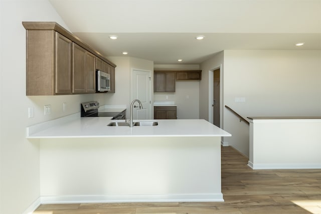 kitchen with light wood-type flooring, stainless steel appliances, kitchen peninsula, and sink
