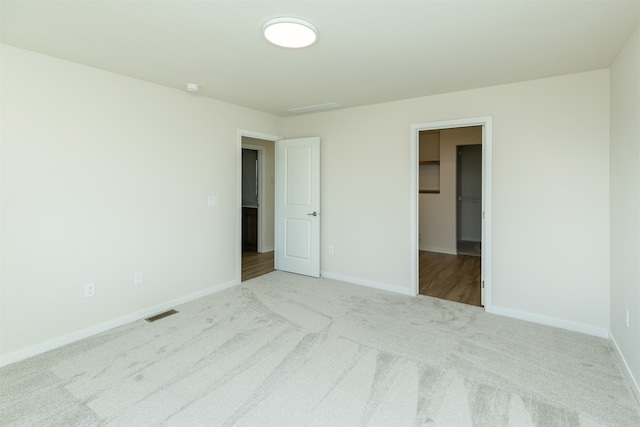 unfurnished bedroom with a closet, a spacious closet, and light colored carpet