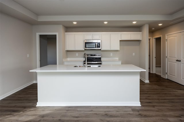 kitchen featuring dark wood-type flooring, stainless steel appliances, a center island with sink, and white cabinets