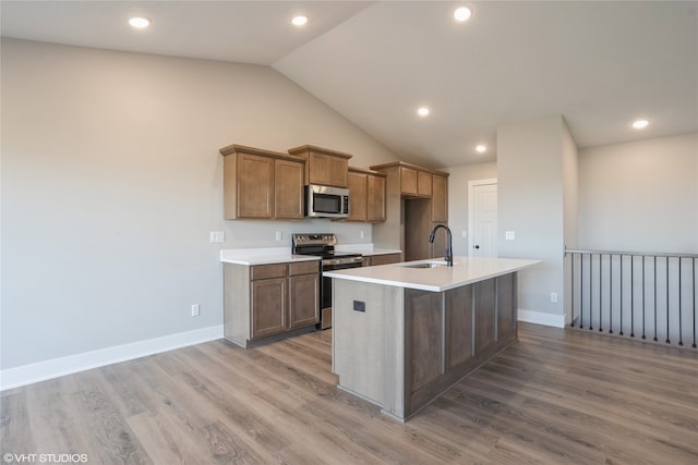 kitchen with light hardwood / wood-style flooring, an island with sink, sink, vaulted ceiling, and appliances with stainless steel finishes