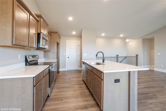 kitchen with appliances with stainless steel finishes, a kitchen island with sink, sink, and light hardwood / wood-style floors