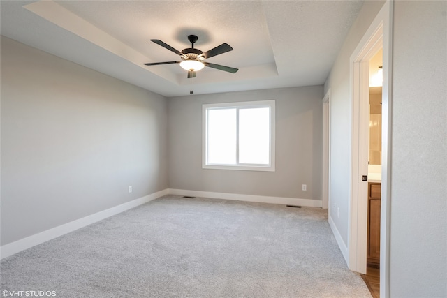 carpeted spare room featuring ceiling fan and a tray ceiling