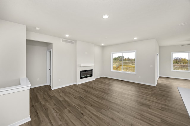 unfurnished living room featuring ceiling fan, a healthy amount of sunlight, and dark hardwood / wood-style floors