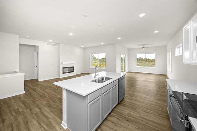 kitchen featuring a center island with sink, stainless steel dishwasher, dark hardwood / wood-style floors, gray cabinetry, and sink