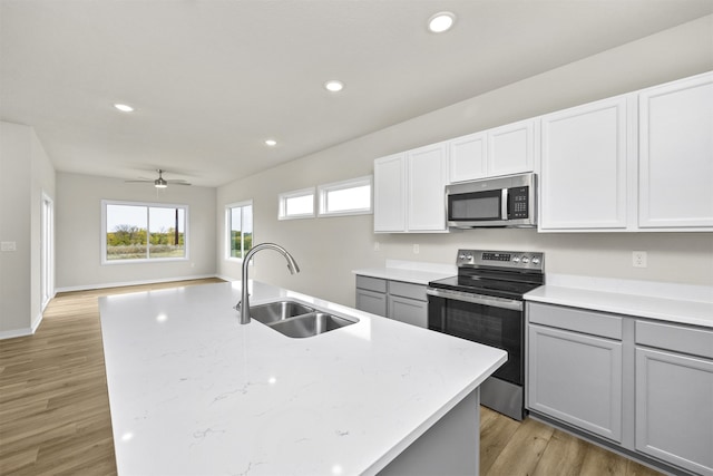 kitchen featuring gray cabinetry, appliances with stainless steel finishes, sink, light wood-type flooring, and an island with sink