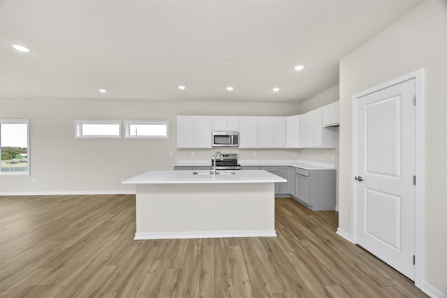 kitchen featuring an island with sink, gray cabinetry, appliances with stainless steel finishes, light wood-type flooring, and white cabinets