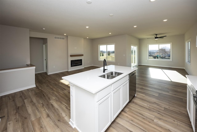 kitchen with stainless steel dishwasher, a kitchen island with sink, sink, white cabinets, and light hardwood / wood-style floors