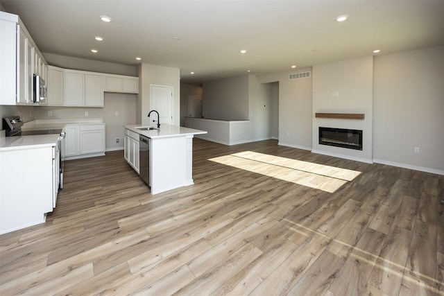 kitchen with a kitchen island with sink, white cabinets, sink, light hardwood / wood-style flooring, and appliances with stainless steel finishes